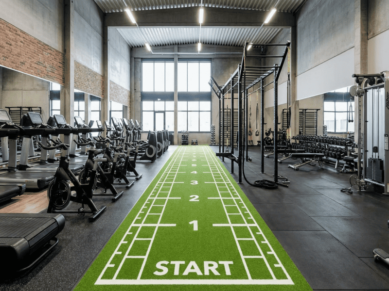 Close-up of artificial turf bubbling and peeling away from a concrete gym floor